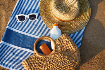 Sunbathing accessories on sandy beach, straw hat beside sunglasses, sunblock lotion in bag for skin protection, summer seaside holiday essentials on striped towel, outdoor UV care on sunny day.