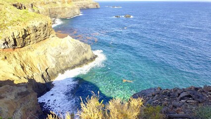 Wall Mural - An ocean bay surrounded by mountainous overhangs with a beautiful blue to turquoise ocean