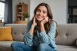 © ThomasLENNE - Happy girl with hand on chin sitting in living room at home