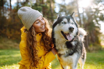 Wall Mural - A young woman walks with her dog in the autumn forest. Husky dog.  Pet owner enjoys walking her dog outdoors.