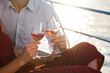 Drinking wine on yacht at sea. Two wineglasses in hands of couple in love at sunset. Man and woman relaxing, traveling and enjoying summer vacation. Intimate romantic dating, celebration. Close up
