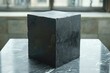 A mysterious dark cube glistens with wetness sitting on a pale marble countertop with soft natural light