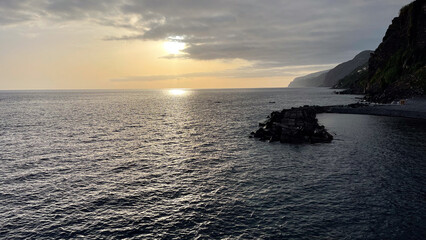 Wall Mural - A serene sunset over the Atlantic Ocean, casting soft light on the water and rocky coastline of Madeira Island