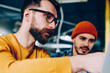 © BullRun - Close up view of skilled male it developer coaching trainee pointing on laptop computer while explaining, hipster guy communicating with friend working on project together showing new app on netbook