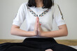 Close up image of woman's hands who is sitting cross-legged, hands folded, on the floor of the room at home To meditate to make the mind calm and relaxed. The room is bright with natural light.