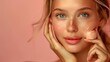 © Athena - Portrait of a young woman with clear skin and freckles applying facial cream on a pink background