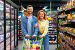 © Home-stock - Happy family husband and wife walking with shopping cart full of grocery, shopping together at supermarket, smiling at camera