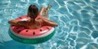© Miss V - a woman in bikini is relaxing in a pool in an inflatable ring looking as a watermelon. Summer leisure