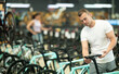 Focused young adult man assessing saddle while choosing bicycle in store, looking for comfort and fit for cycling activities