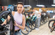 Young woman selects bicycle in modern sporting goods store, checking wheel quality