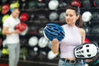 Attentive sporty woman buyer choosing safe bicycle helmet in big sports store