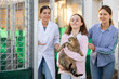 Happy caring preteen girl holding adopted big gray tabby tomcat in arms while standing with mother and female worker of shelter outdoors near kennels 