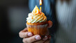 Womans hand holding birthday cupcake with candle. Close up cupcake