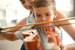 © New Africa - Young woman teaching little boy to play violin indoors, closeup