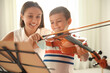 © New Africa - Young woman teaching little boy to play violin indoors