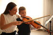 © New Africa - Young woman teaching little boy to play violin indoors