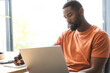 © Wavebreak Media - At home, African American male wearing an orange shirt, working on laptop