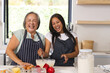 © Wavebreak Media - Asian grandmother and biracial teen laugh in aprons as they cook at home