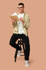 Poster - Handsome young man sitting on chair and reading book on beige background