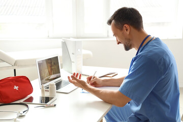 Canvas Print - Handsome doctor video chatting with patient on laptop in office