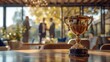 A gold trophy sits on a wooden table in the foreground with an out of focus background of a restaurant with people talking.