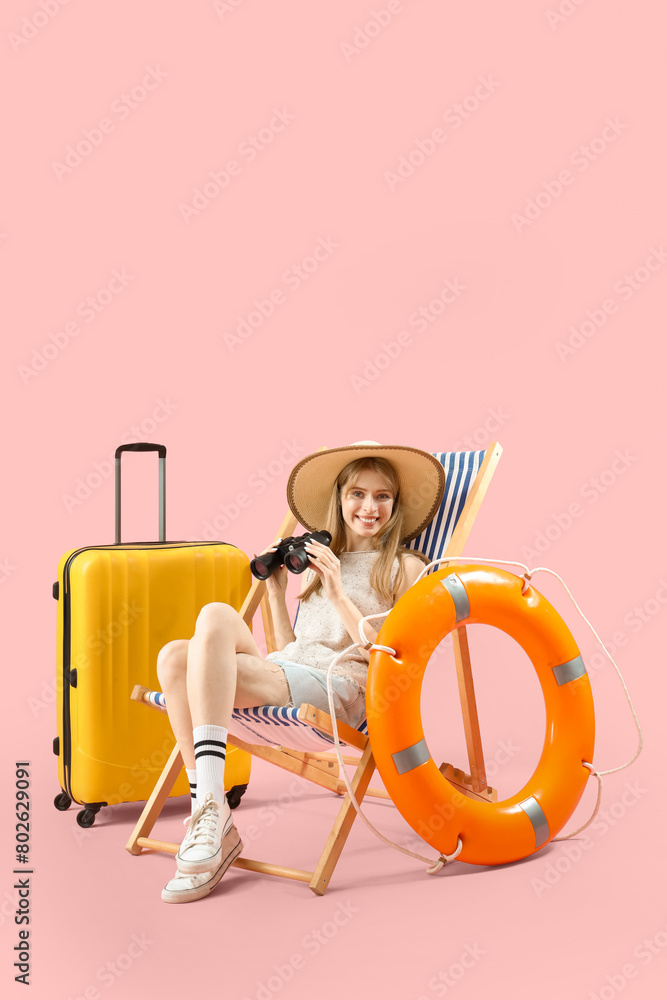 Female tourist with binoculars in deck chair on pink background