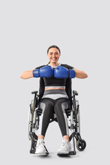 Wall Mural - Sporty young woman in wheelchair with boxing gloves on light background