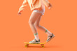 Legs of beautiful young woman on skateboard against orange background