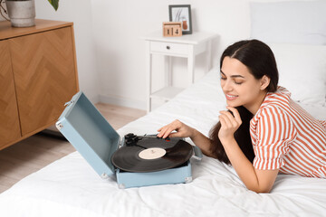 Sticker - Beautiful young happy woman with record player and vinyl disk lying on bed at home