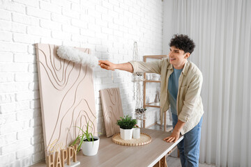 Sticker - Young man cleaning painting with pp-duster at home