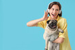 Young woman in headphones holding cute pug dog on blue background