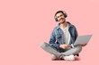 Young bearded man in headphones with laptop listening to music on pink background