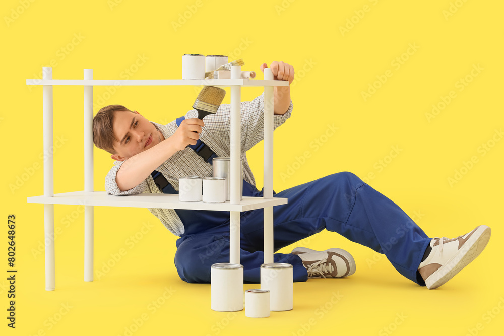 Male decorator painting shelf unit on yellow background