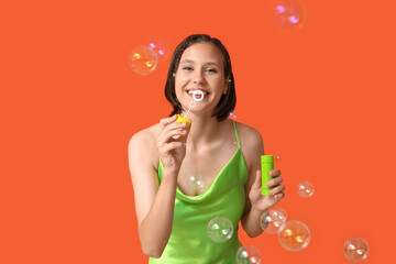 Wall Mural - Teenage girl blowing soap bubbles on orange background