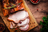 Fototapeta Na sufit - Baked festive pork butt or ham with herbs, spices and cranberries for sauce, served and sliced on cutting board, rustic wooden table background, top view