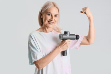 Sticker - Mature woman massaging her arm with percussive massager on light background