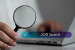 A man hold a magnifier to find job with search icon bar, seeking into right job. Behind that has used laptop put in front of him. Data search technology search engine optimization. HRM concept