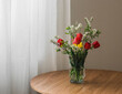 A spring bouquet of tulips and spirea in a glass vase on a round wooden table in the living room