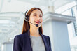 Smiling asian businesswoman woman consultant wearing microphone headset of customer support phone operator at walkway in the office area.
