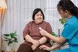 A young Asian female nurse or medical assistant uses a stethoscope to perform a physical examination on a disabled Asian woman with Down syndrome.