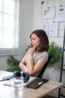 © Wasana - A woman sits at a desk with a laptop and a tablet. She is looking at the laptop screen and she is deep in thought.