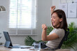 © Wasana - A woman is sitting at a desk with a laptop and a cup of water. She is smiling and she is happy