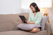 © Wasana - A woman is sitting on a couch with a tablet. Wearing headphones and enjoying her music.