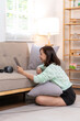 © Wasana - A woman is sitting on the floor in front of a couch, holding a tablet