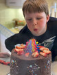 Boy blows out candles on a festive chocolate birthday cake