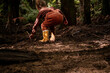 Child picking up stick in forest with muddy yellow boots