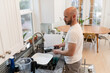 Man rinsing dishes in sunny kitchen