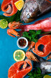 Fresh seafood assortment on blue. Trout steaks, beaked redfish and shrimps. Cooking ingredients. Top view