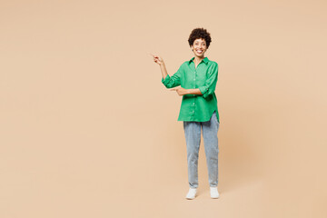Wall Mural - Full body young woman of African American ethnicity wear green shirt casual clothes point index finger aside indicate on area isolated on plain pastel light beige background studio. Lifestyle concept.