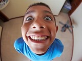 Fototapeta  - Distorted fish-eye lens view of a smiling boy looking into the camera creates a playful and humorous effect.